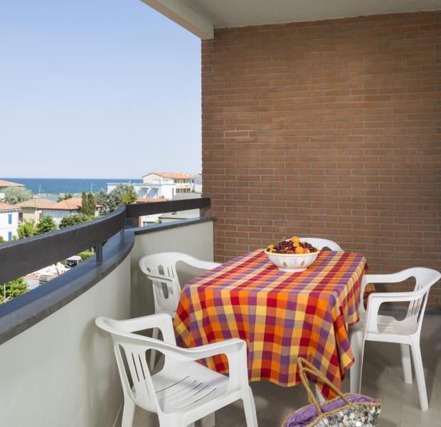 Balcony with sea view, colorful table, and white chairs.