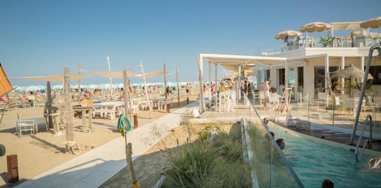 Crowded beach with bar and pool, under a clear sky.