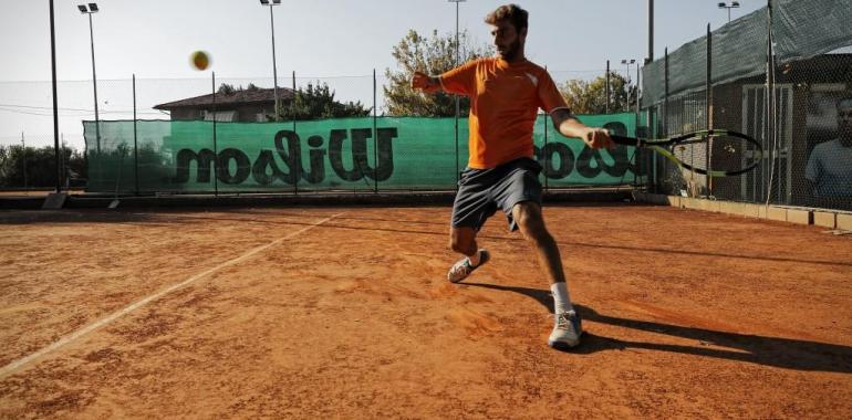 Giocatore di tennis colpisce la palla su un campo in terra rossa.